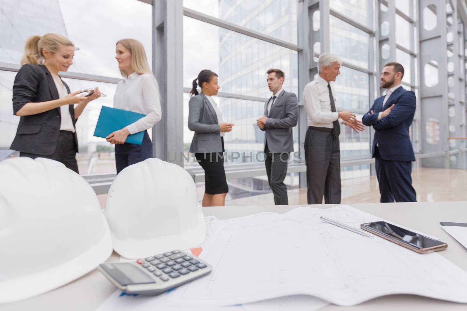 Business people team discuss construction issues , hardhat , blueprint , contract , documents , calculator on office table