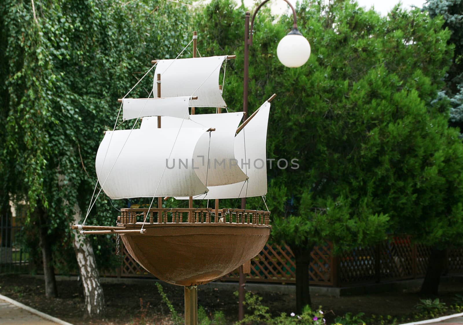 A sailboat made of stone and wood is mounted on a pedestal against the background of trees.