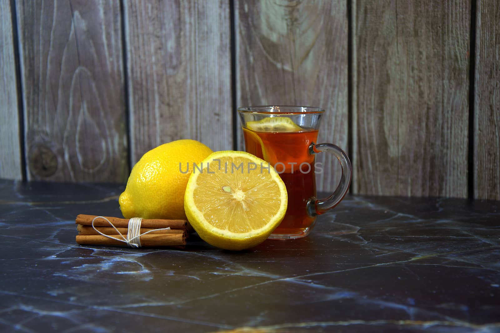 Cinnamon sticks, two lemons and a glass of tea with a slice of lemon.