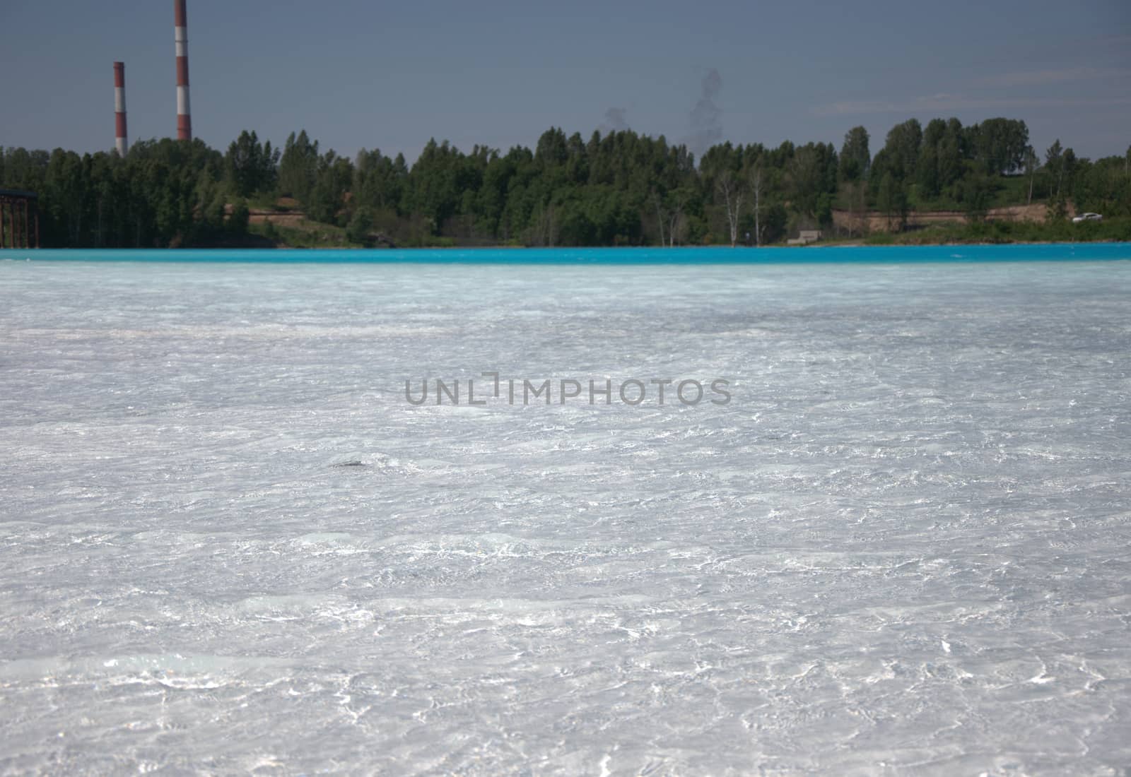 Forest lake with white-blue water, in the background pipes of an old plant.