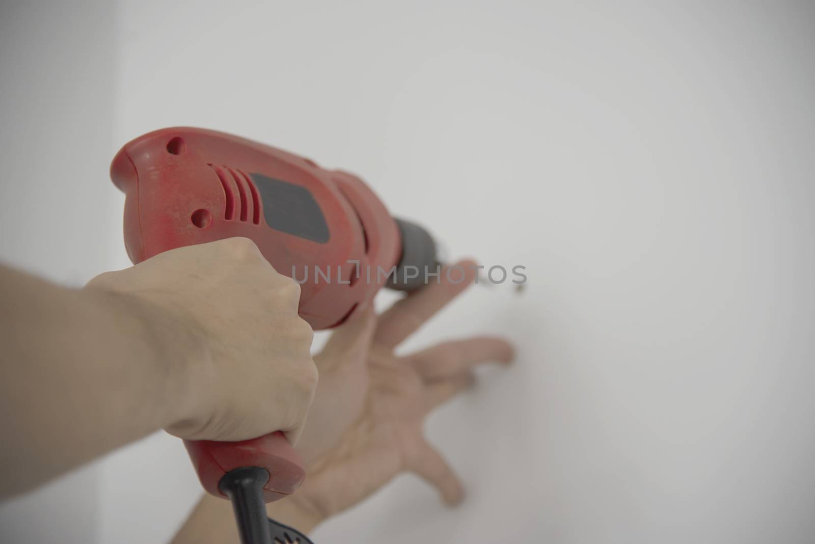 Man using hand drill device for installing home furniture at new white wall - people DIY home furniture installation concept by pairhandmade