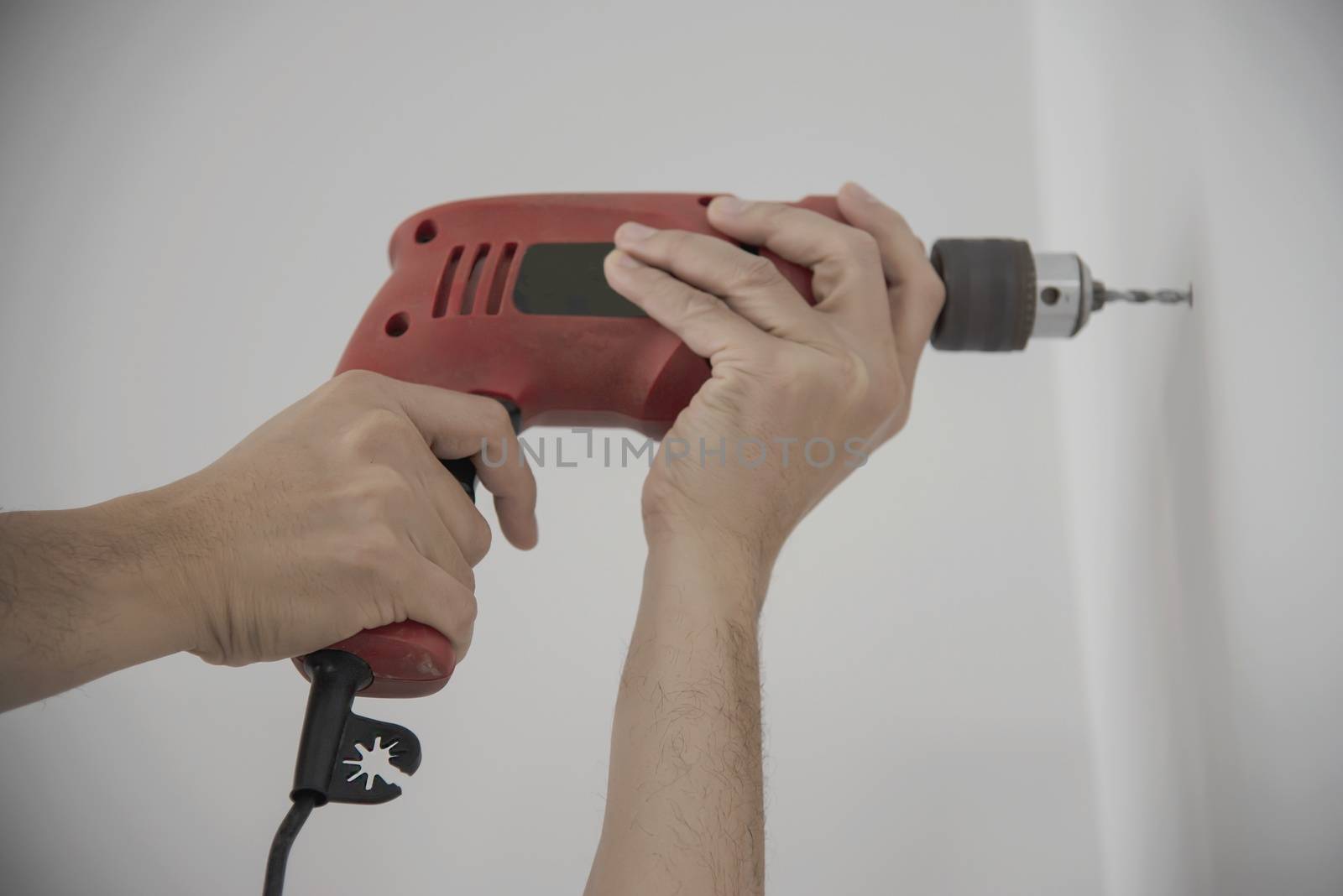 Man using hand drill device for installing home furniture at new white wall - people DIY home furniture installation concept