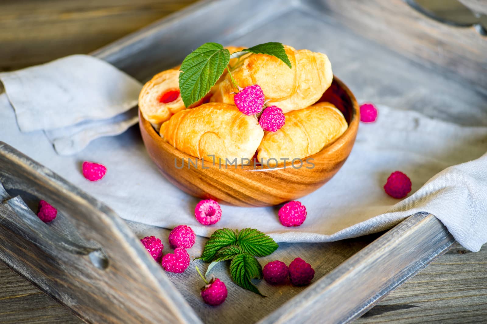 Croissants with raspberries on a wooden tray. The concept of a wholesome breakfast