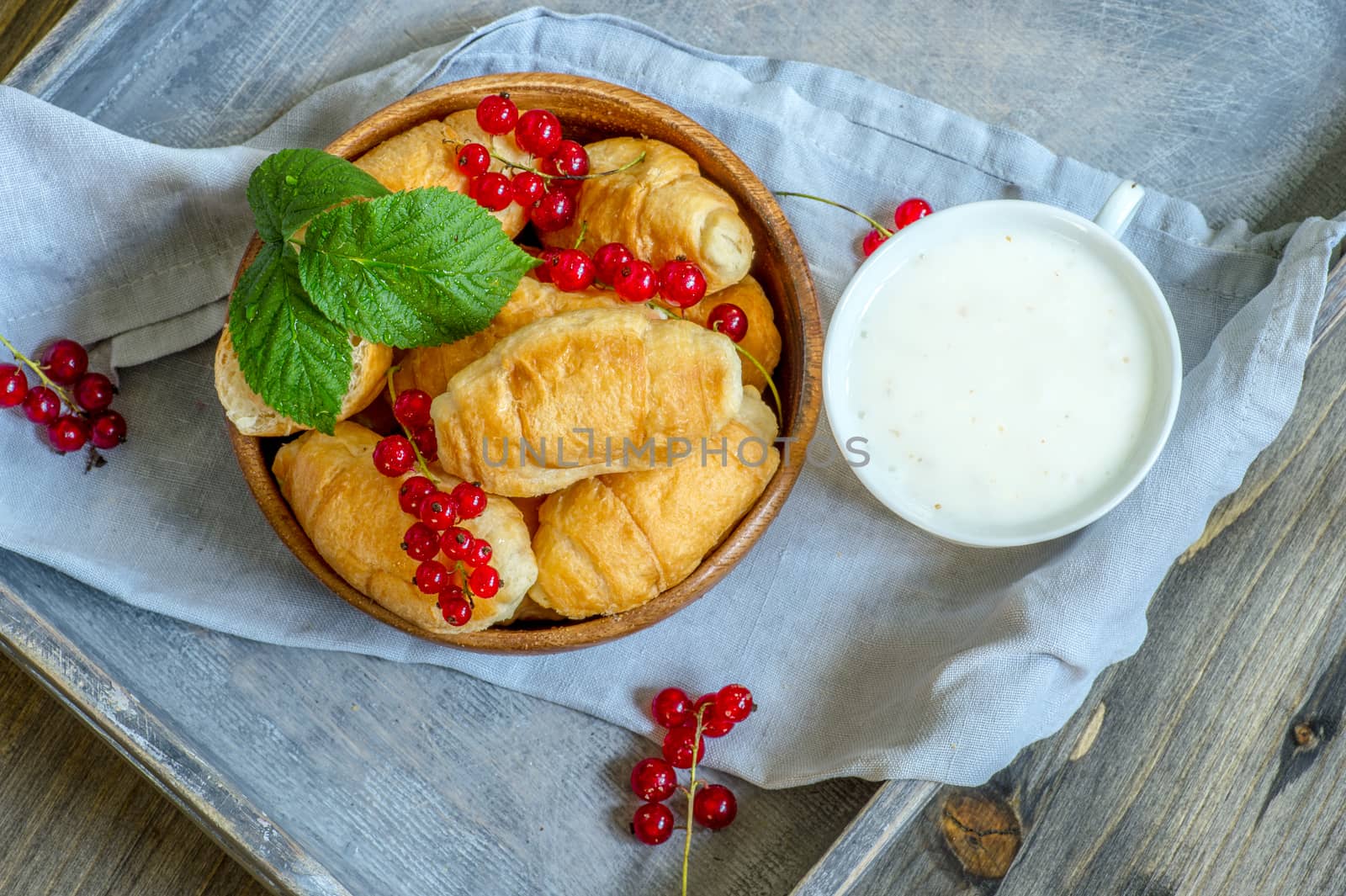 Croissants with currant berries on a wooden tray. The concept of a wholesome breakfast