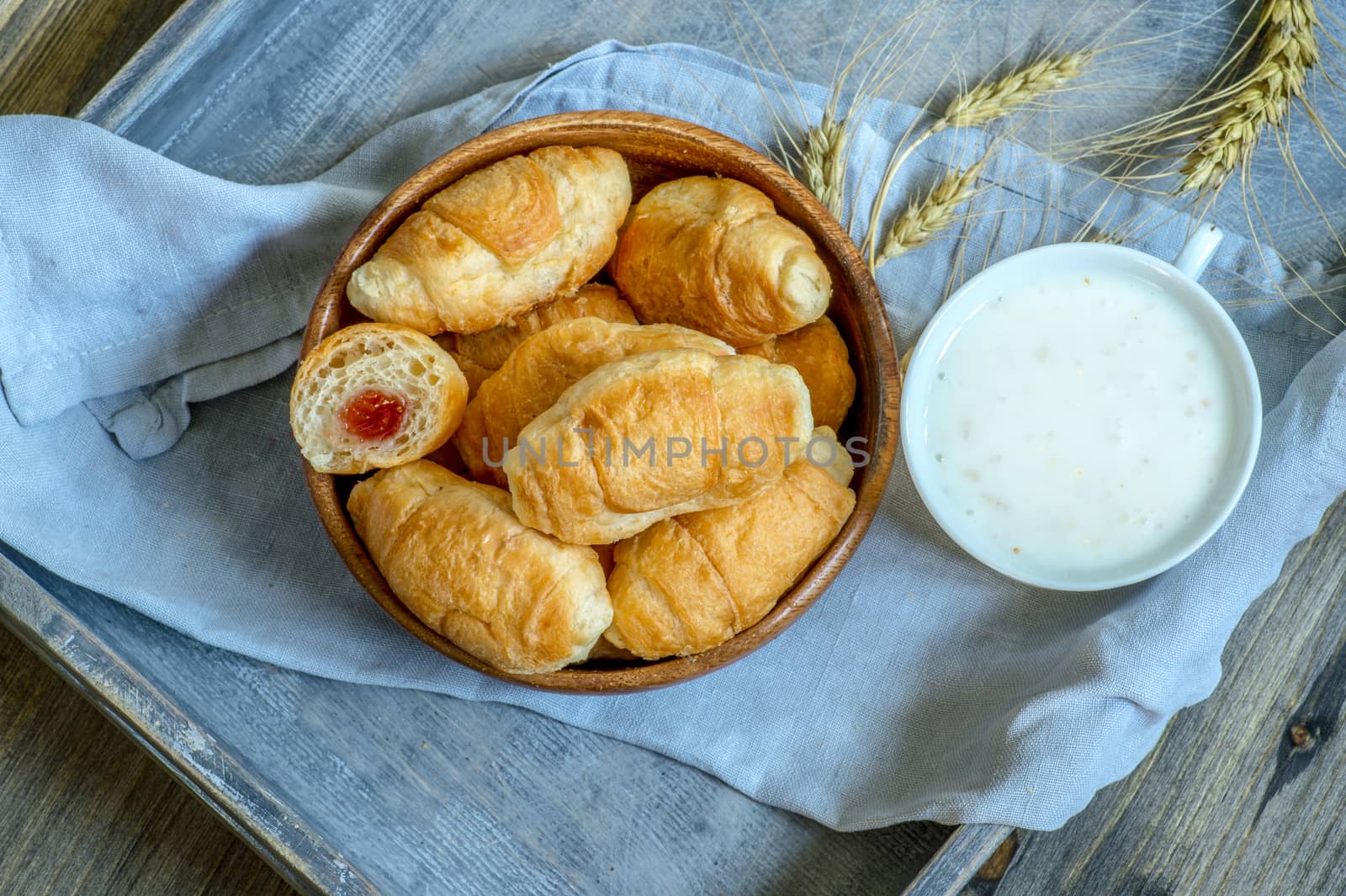 Croissants, a cup with kefir and ears of grain on a wooden tray. The concept of a wholesome breakfast