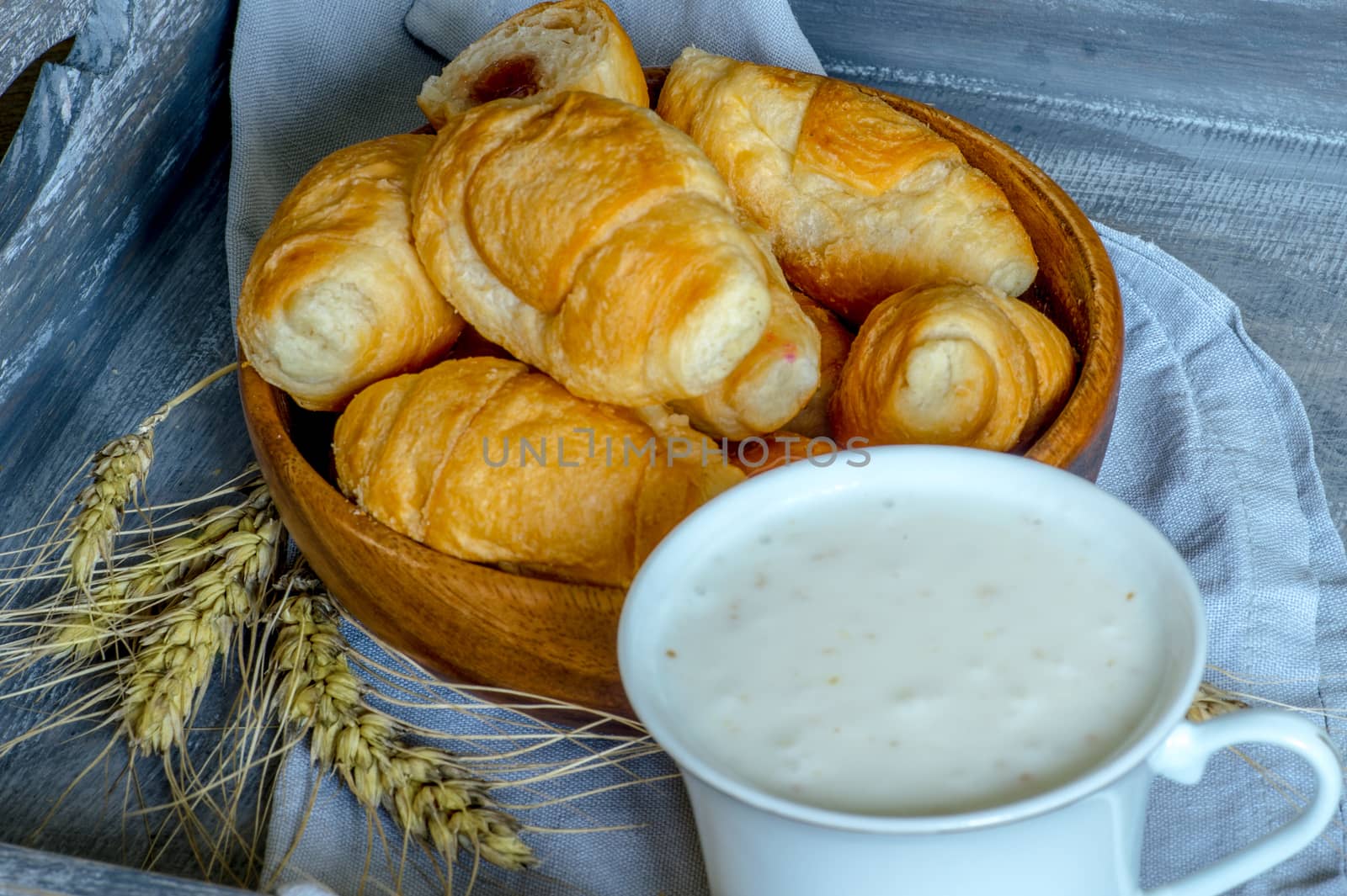 Croissants, a cup with kefir and ears of grain on a wooden tray. The concept of a wholesome breakfast