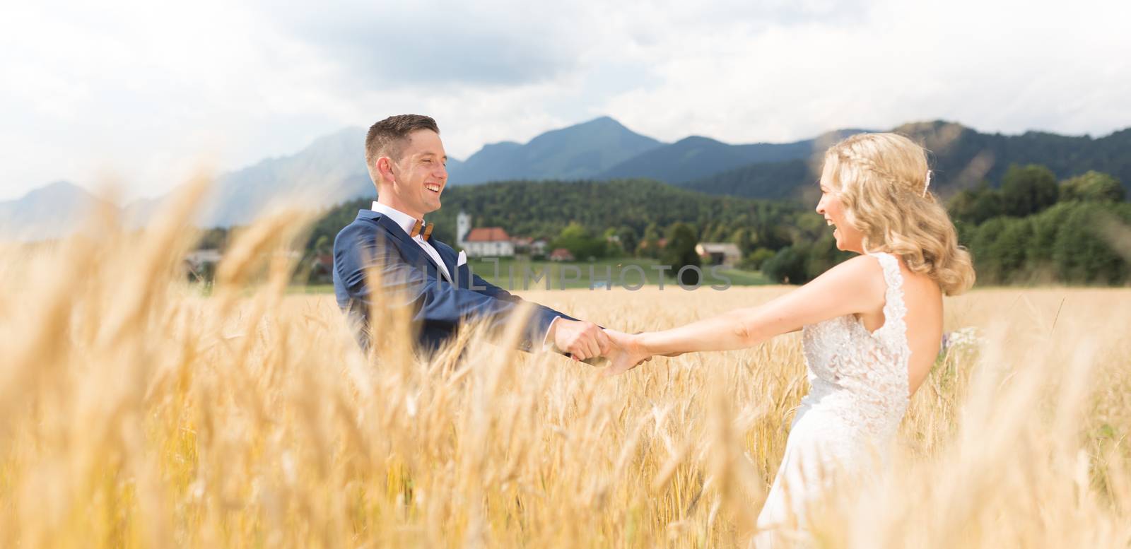 Groom and bride holding hands in wheat field somewhere in Slovenian countryside. Caucasian happy romantic young couple celebrating their marriage.