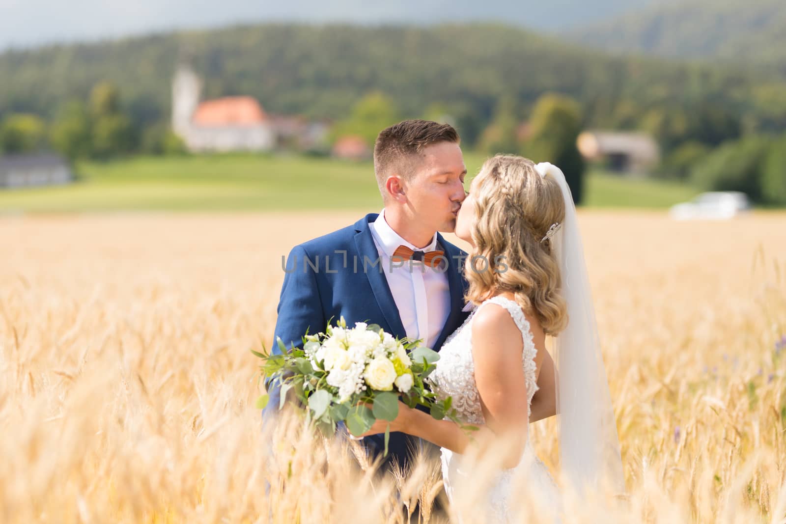 Bride and groom kissing and hugging tenderly in wheat field somewhere in Slovenian countryside. by kasto