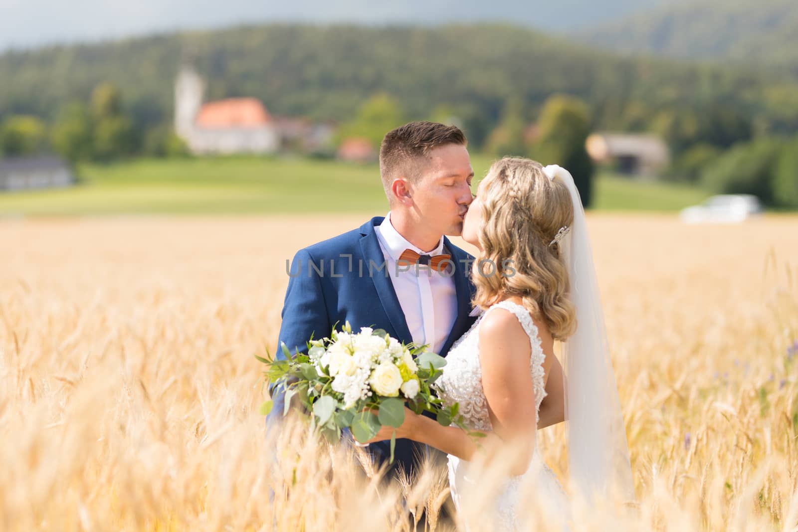 Bride and groom kissing and hugging tenderly in wheat field somewhere in countryside in Slovenian . Caucasian happy romantic young couple celebrating their marriage.