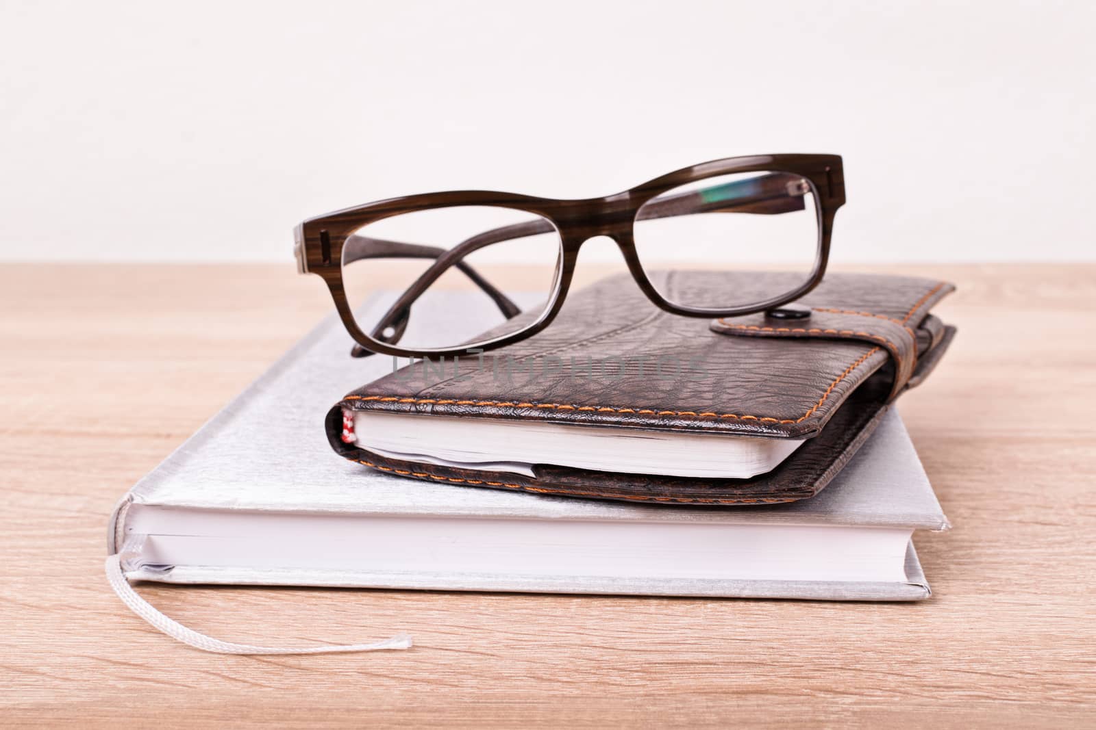 I left my glasses and notes on the table. Notebook, planner and glasses on top of each other placed on a wooden table.