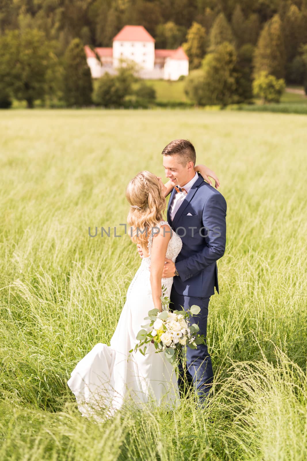 Newlyweds hugging tenderly in meadow in front of Strmol castle in Slovenian countryside. Caucasian happy romantic newlyweds celebrating their marriage.