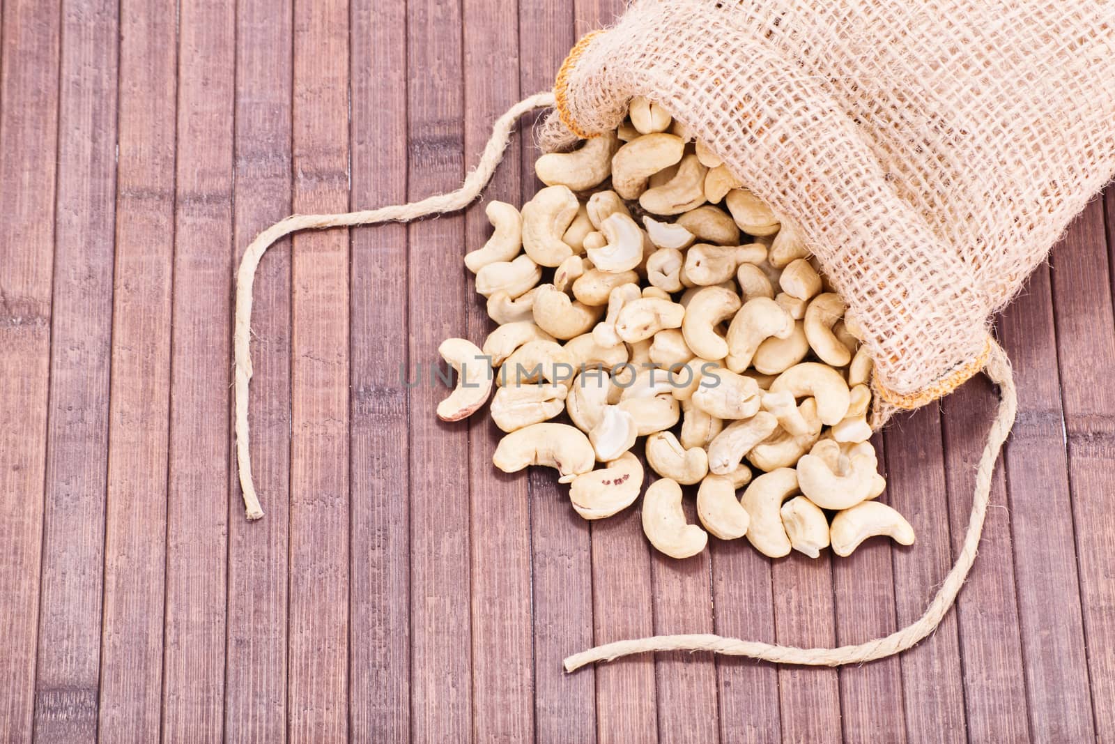 Close up shot of cashews in a burlap sack spilled on wooden background.