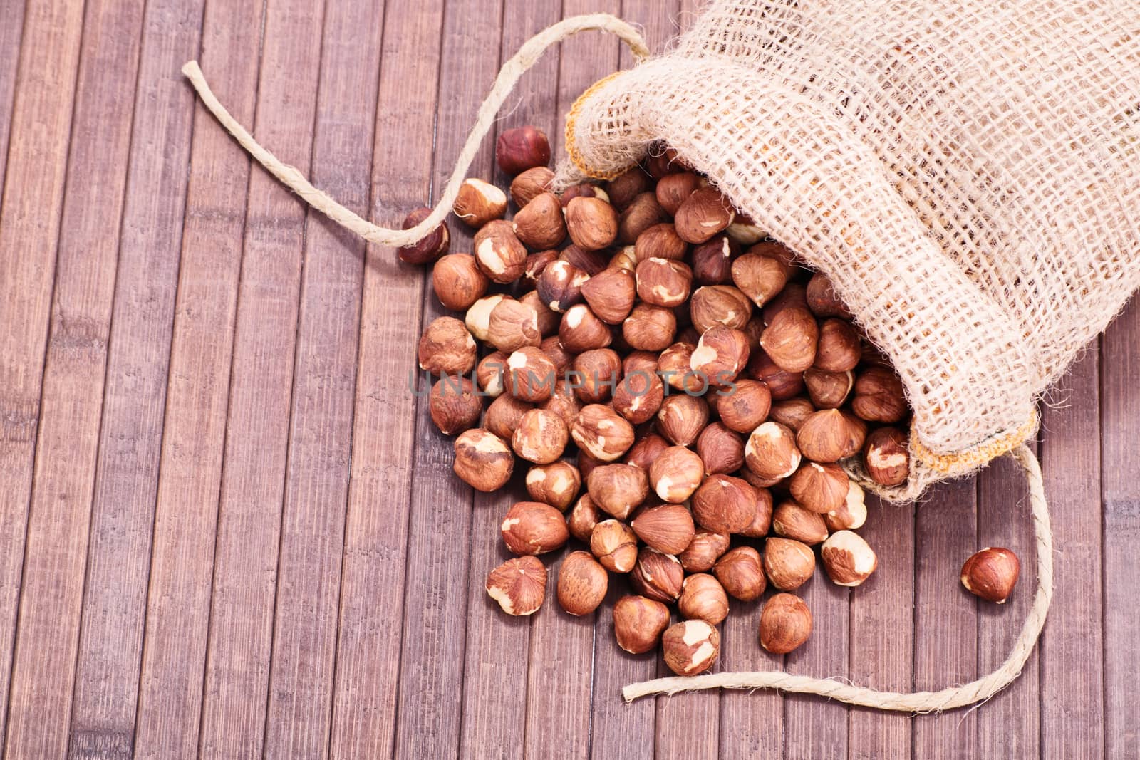 Close up shot of hazelnuts in a burlap sack spilled on wooden background.