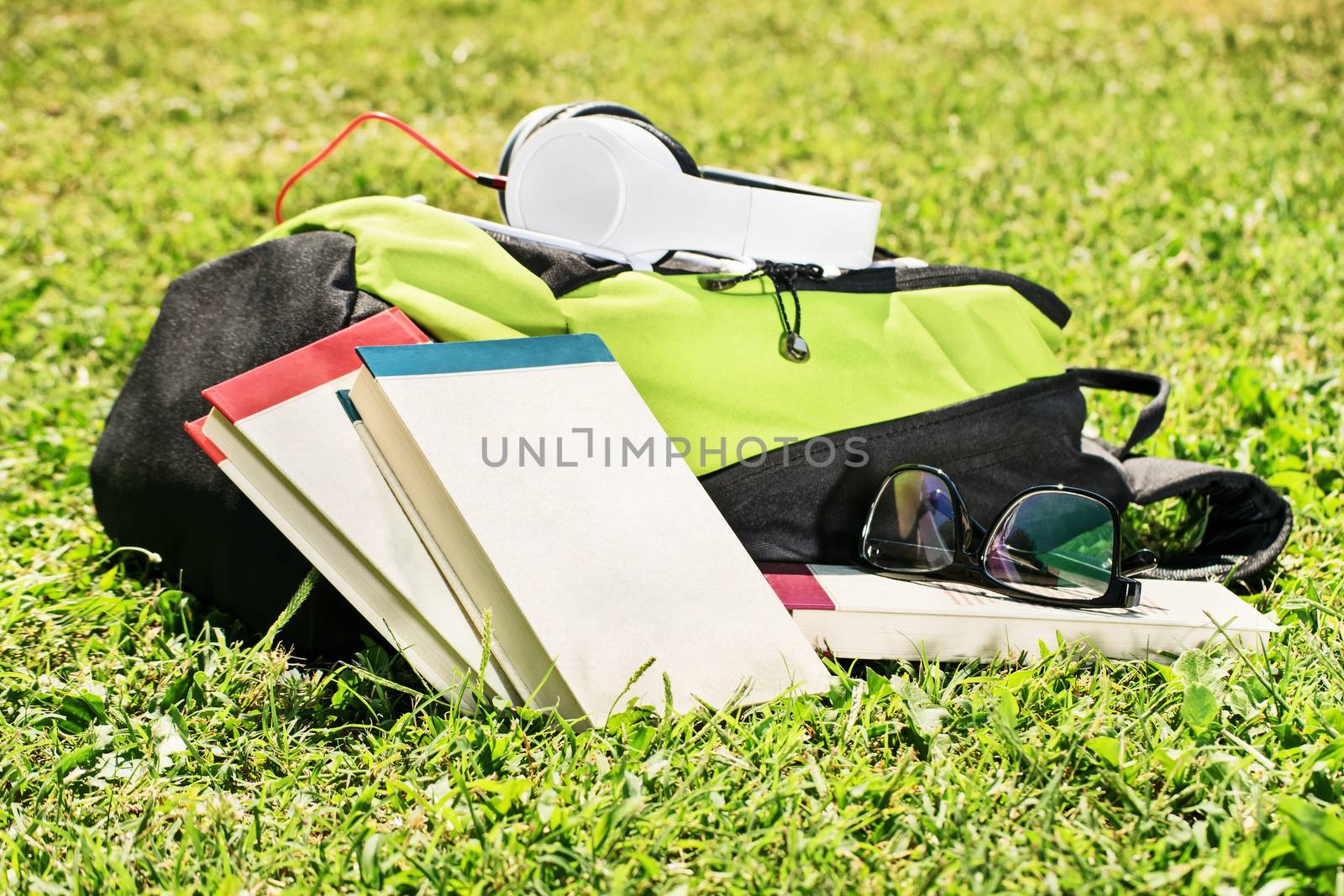 Taking a break after studies. Student backpack with books scattered around, glasses and headphones on a green grass.