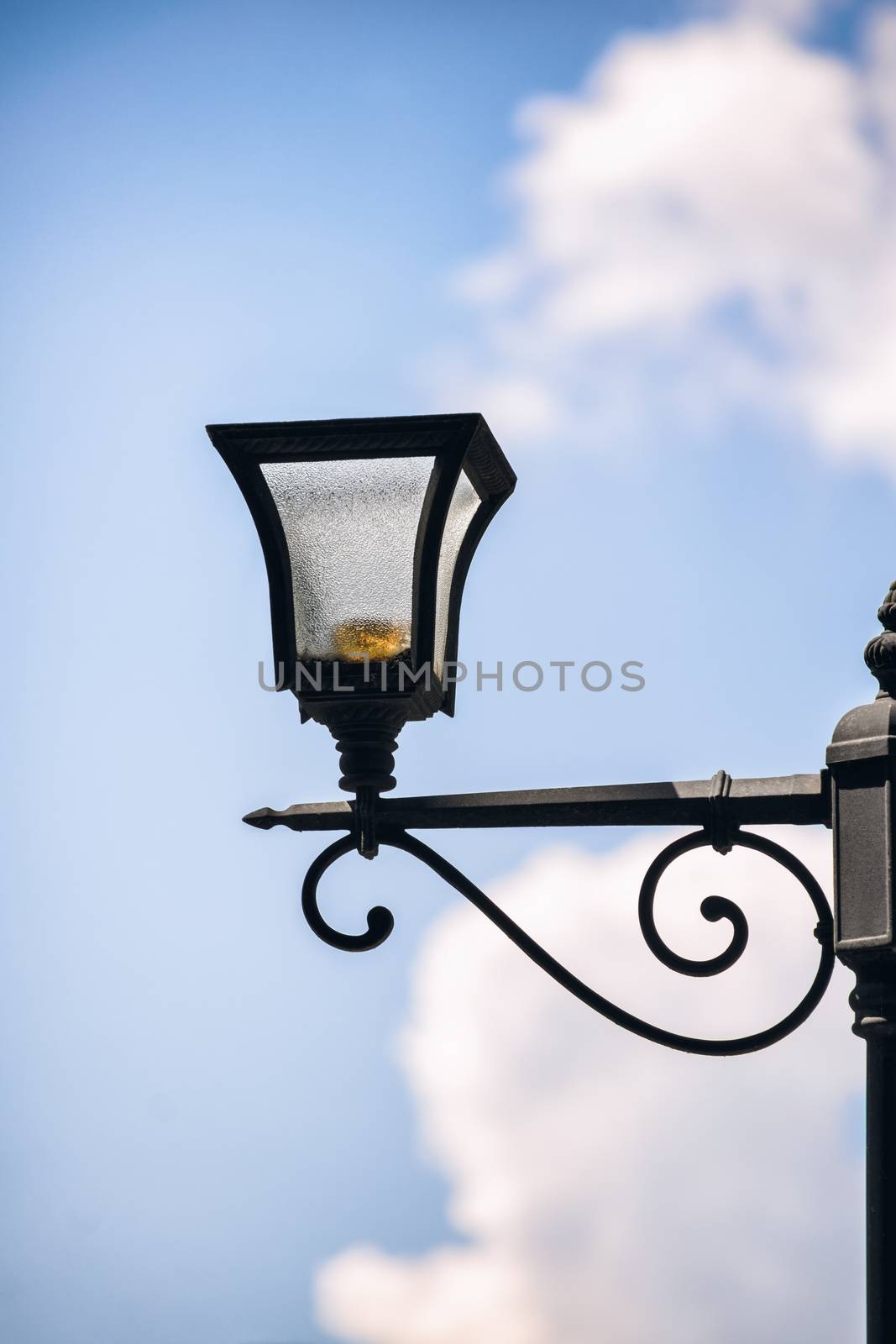 Close up shot of a street lantern under a cloudy blue sky.