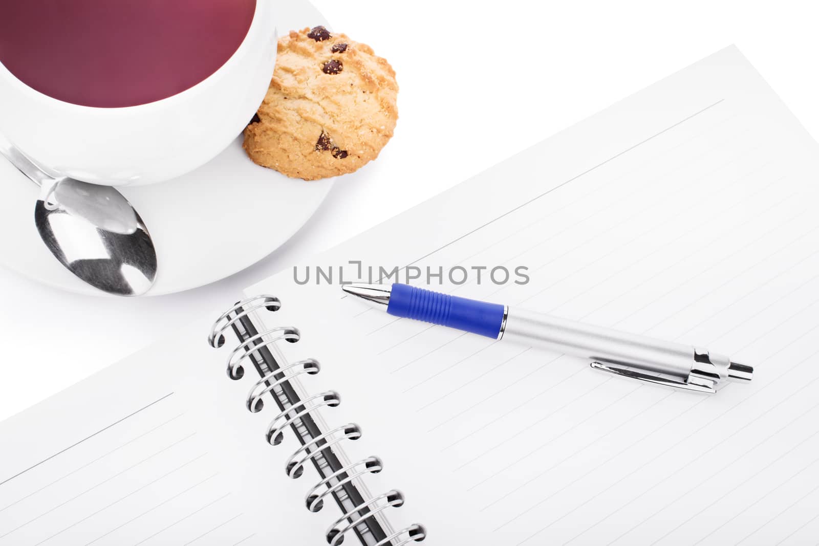 Pen and notebook with a cup of tea, chocolate chip cookie and a small spoon, isolated on white background.