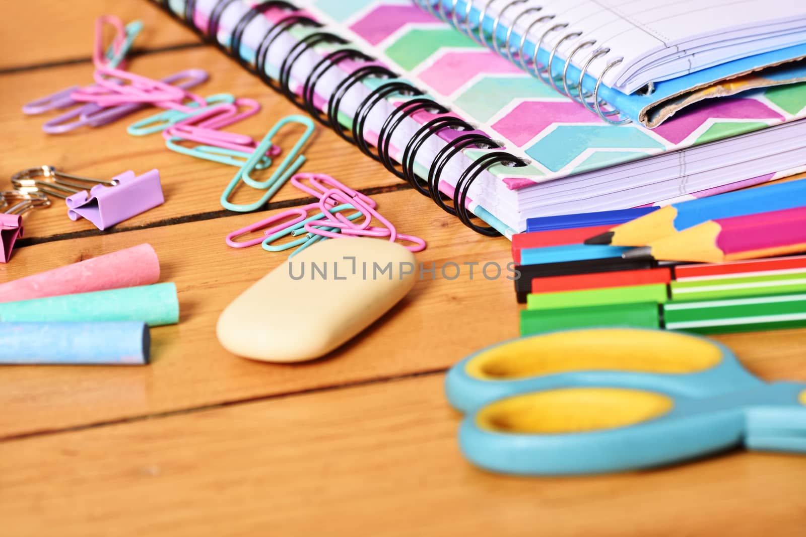 Close up shot of pastel colored girl school stationary on wooden background.