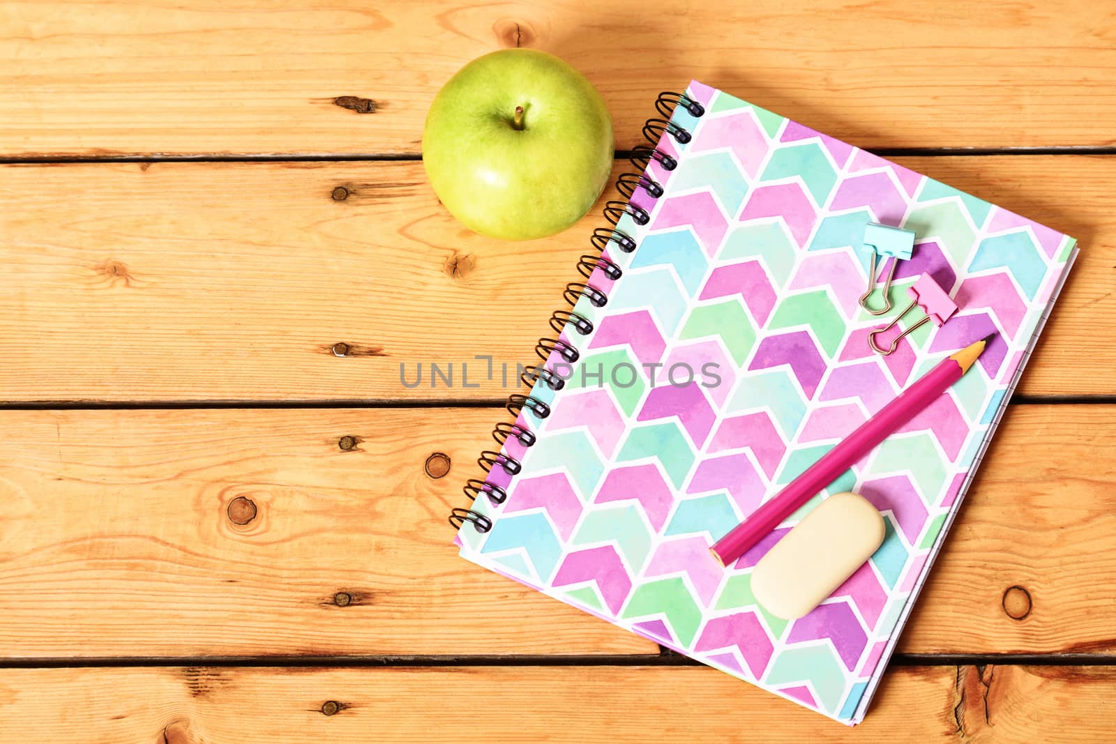 Pink notebook and apple on wooden background by Mendelex