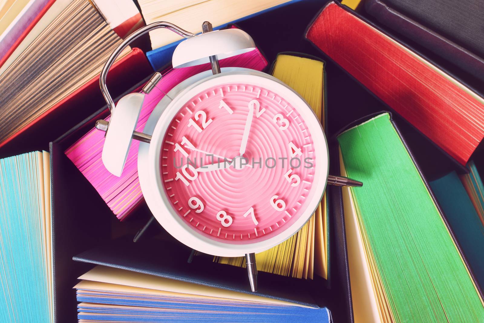 Close up shot of a cute alarm clock on top of open books with multicolored sprayed edges.
