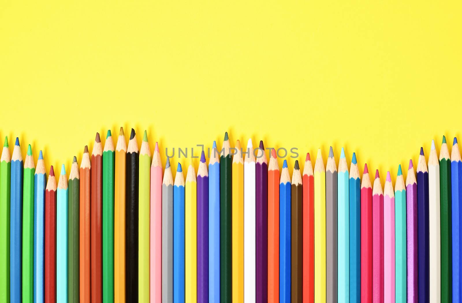 Colorful coloring pencils displayed in a wave on yellow background.