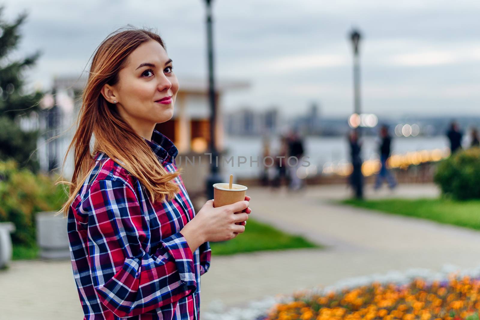 Beautiful young woman holding coffee cup and smiling in the park by Seva_blsv