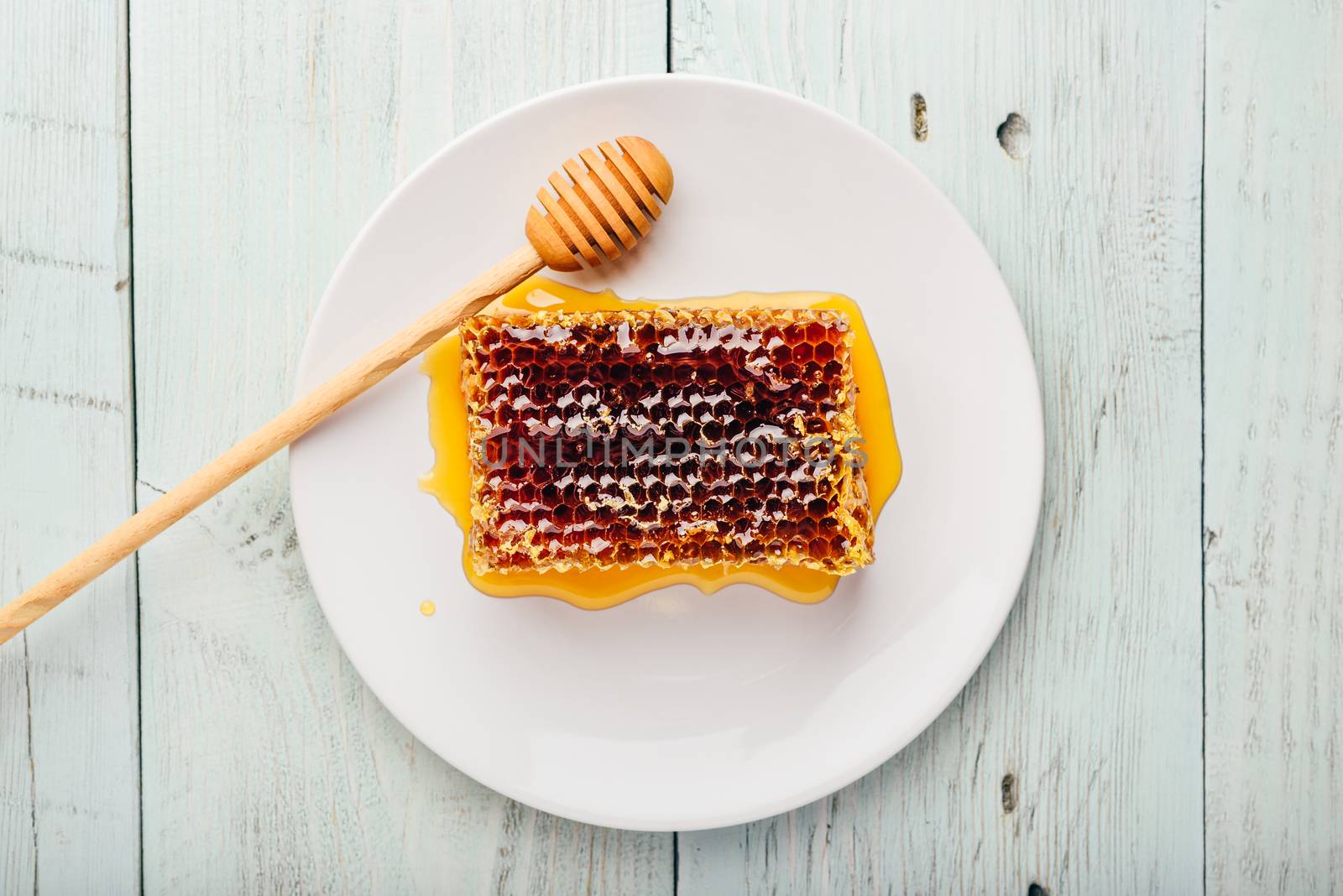 Top view of delicious yummy honeycomb on bright plate with honey dipper over light wooden background