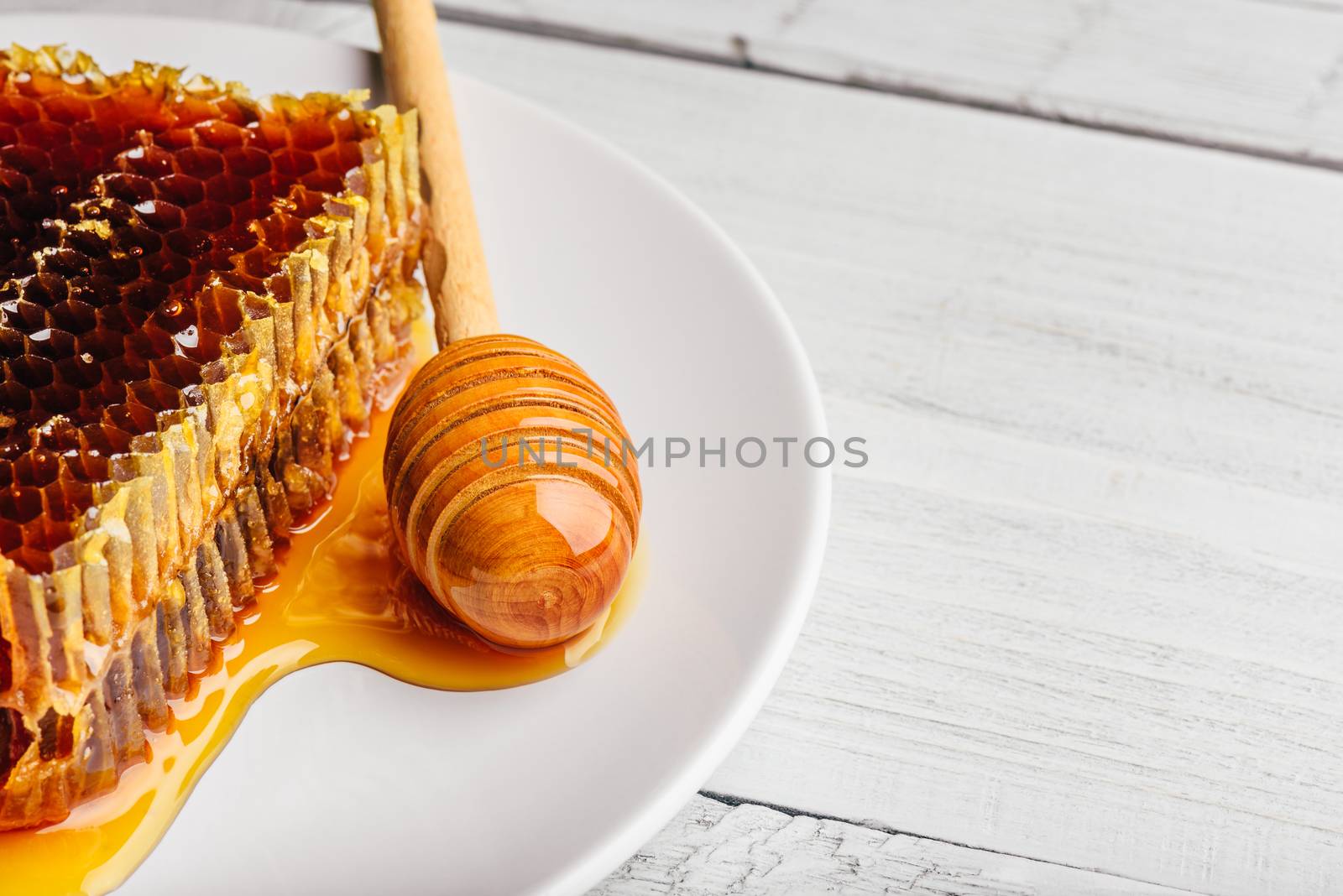 Delicious honeycomb on white plate with wooden honey dipper