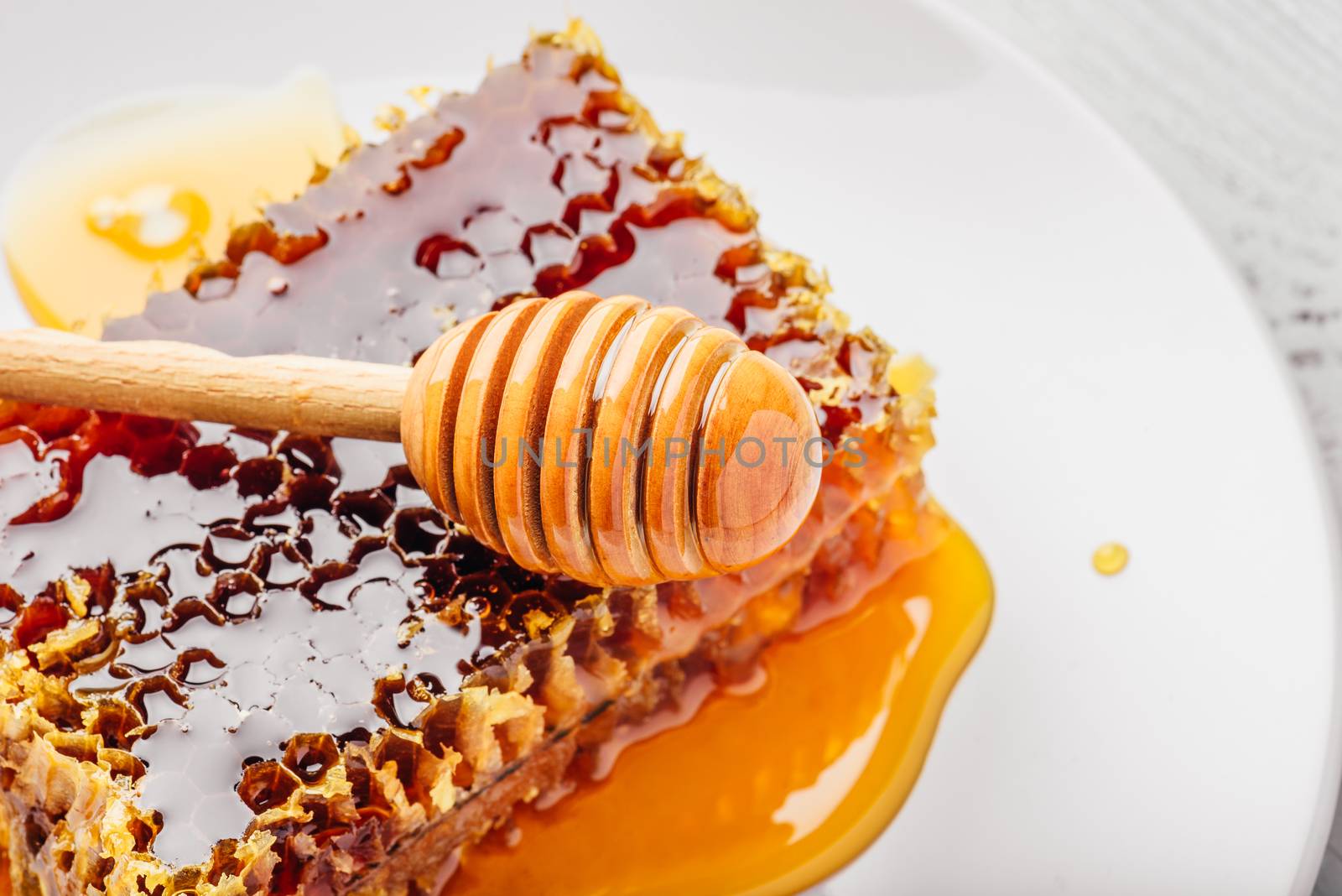 Delicious honeycomb on white plate with wooden honey dipper