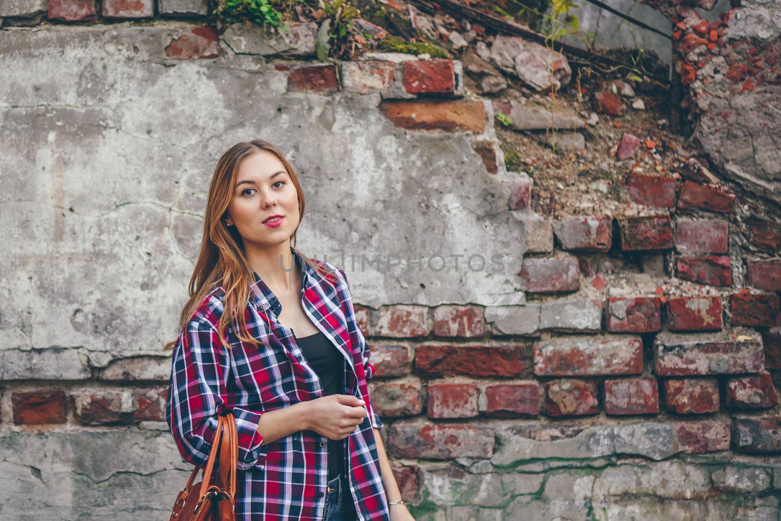 Beautiful girl is looking at camera and standing against brick wall