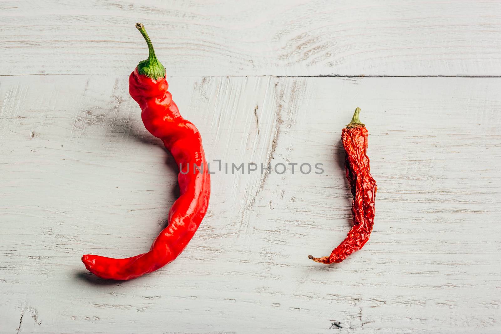 Two red chili peppers, fresh and dry, over wooden background