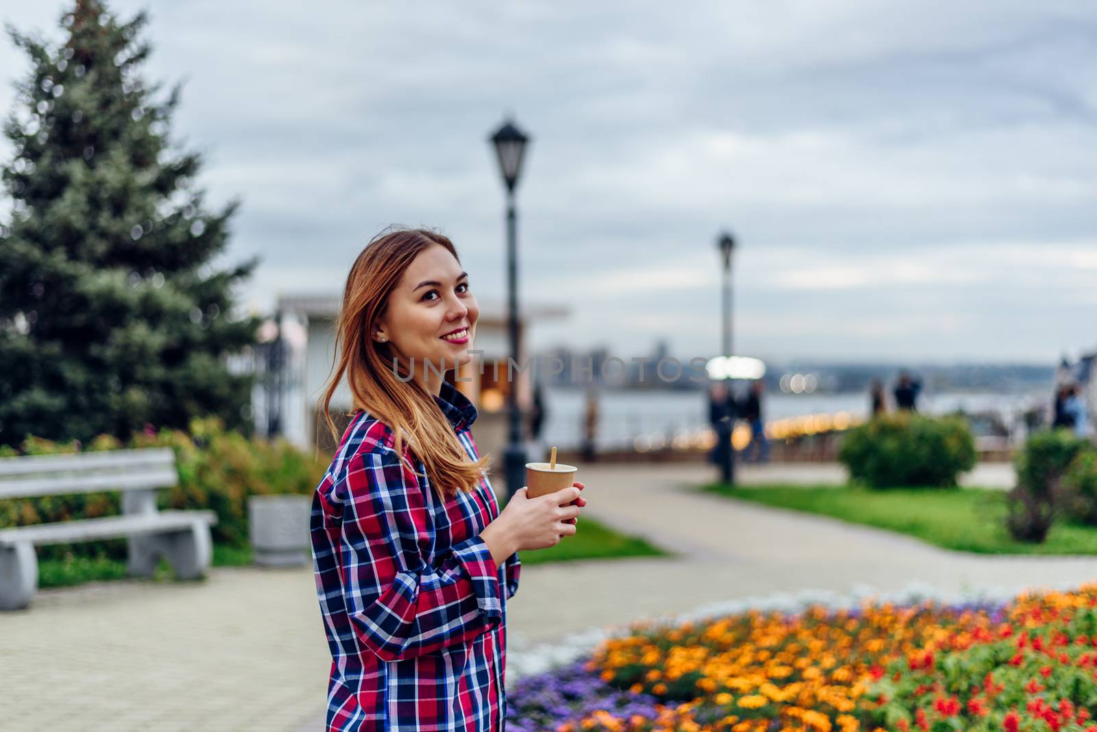 Coffee on the go. Beautiful young woman holding coffee cup and smiling in the park