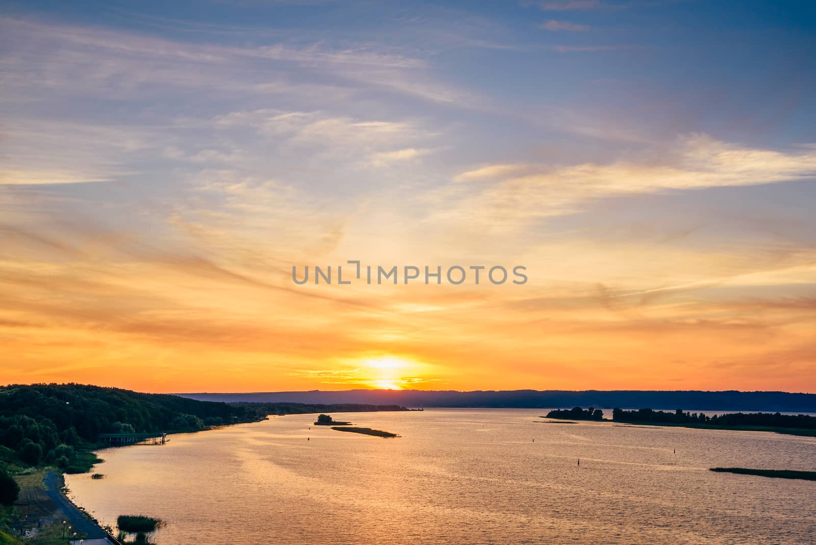 Summer sunset on river shore with orange sky.