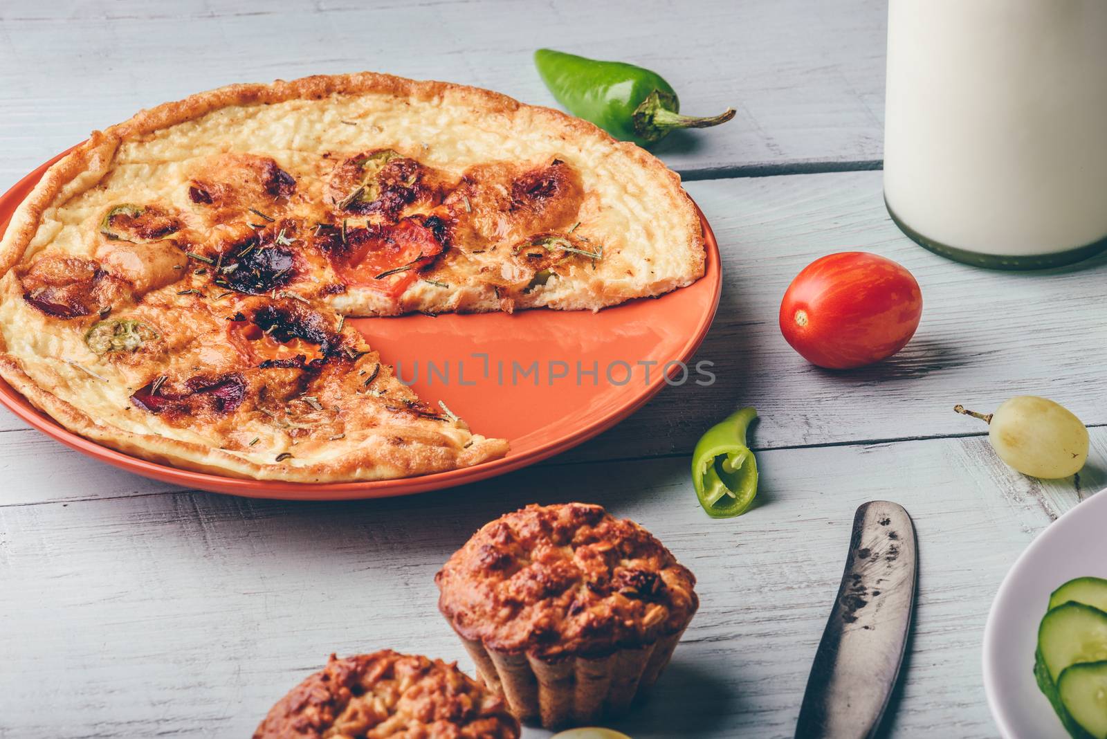 Frittata with chorizo, tomatoes and chili peppers on plate and muffins over light wooden background.