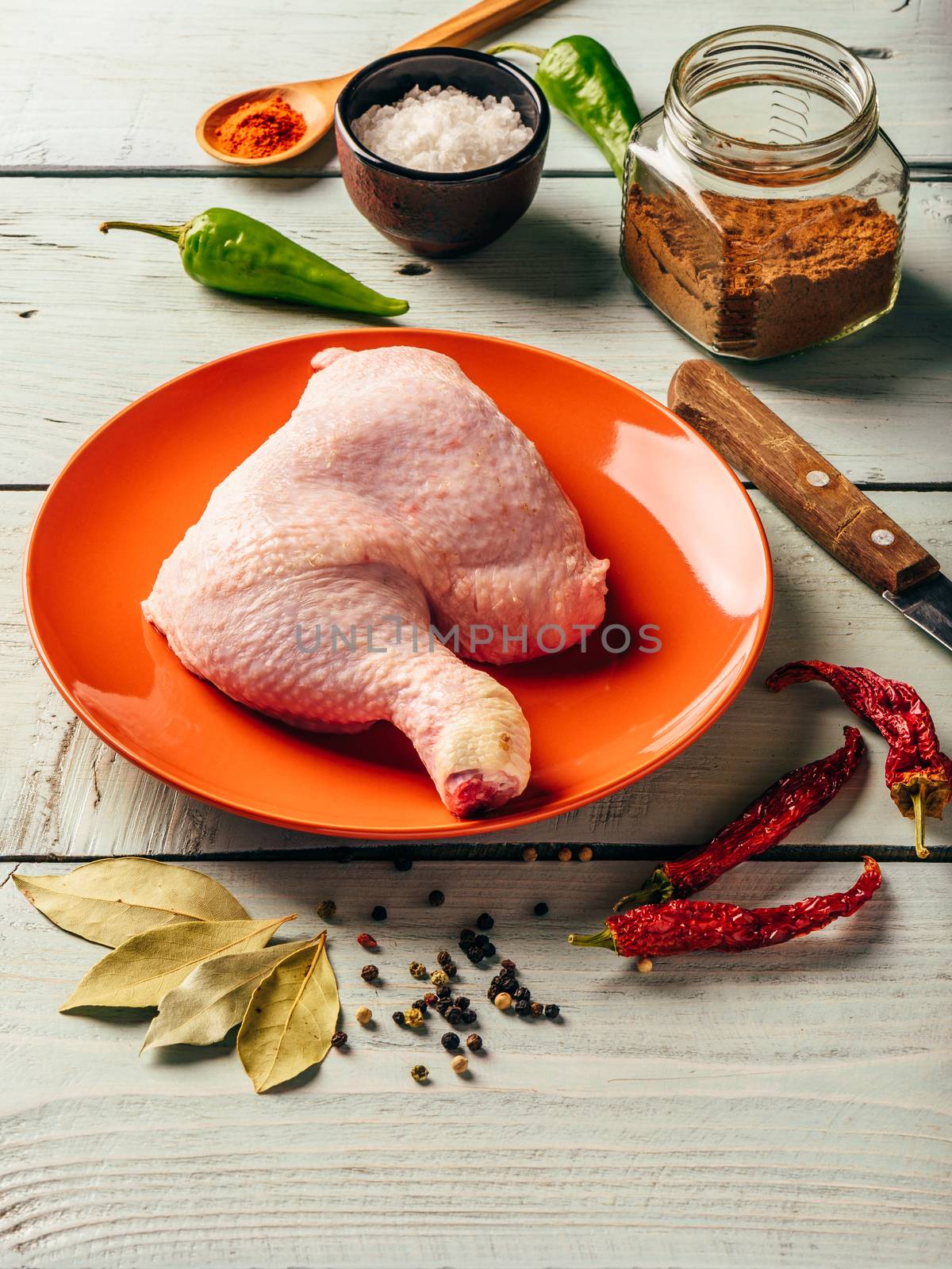 Chicken leg quarter on orange plate over wooden surface with different spices