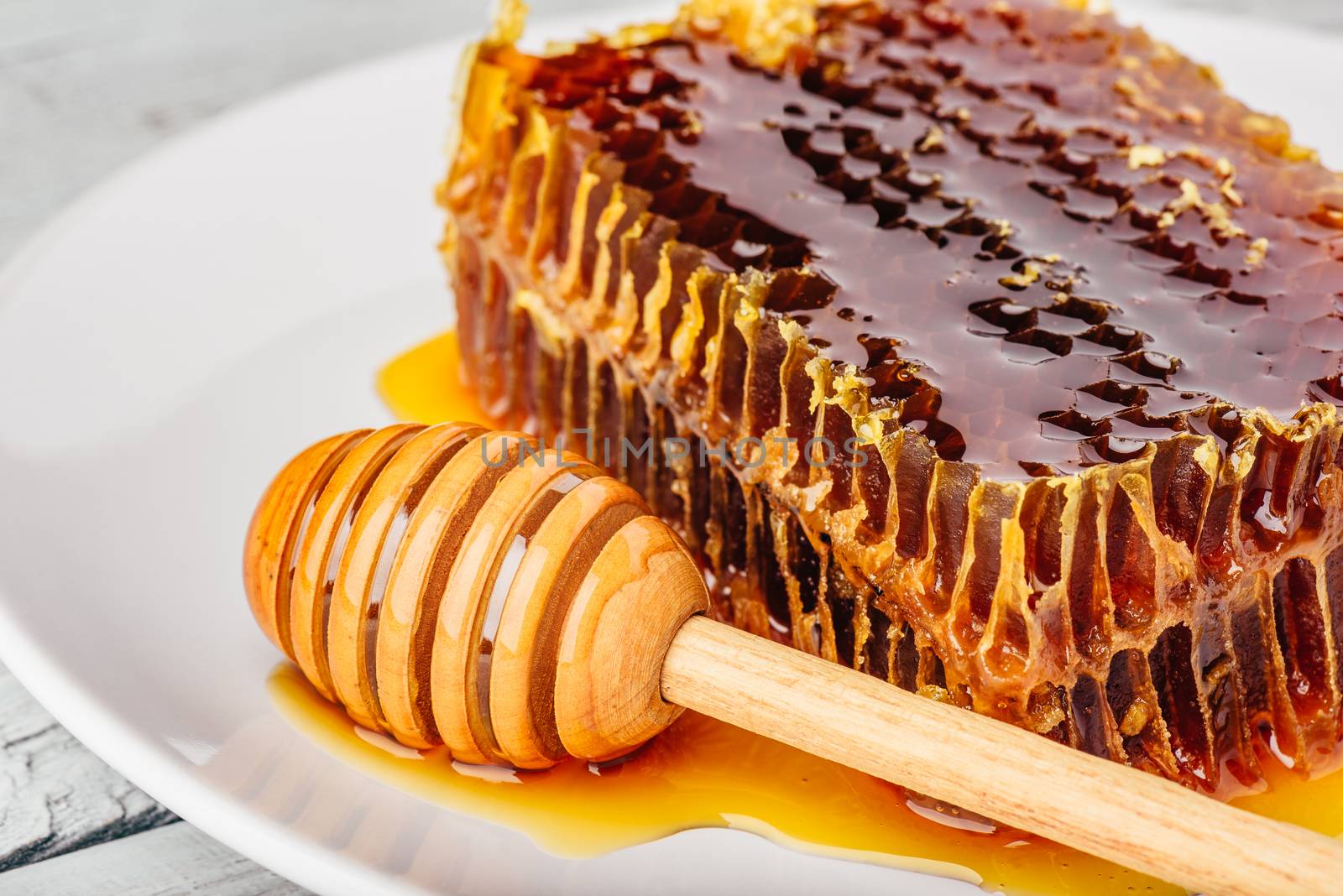 Delicious honeycomb on white plate with wooden honey dipper