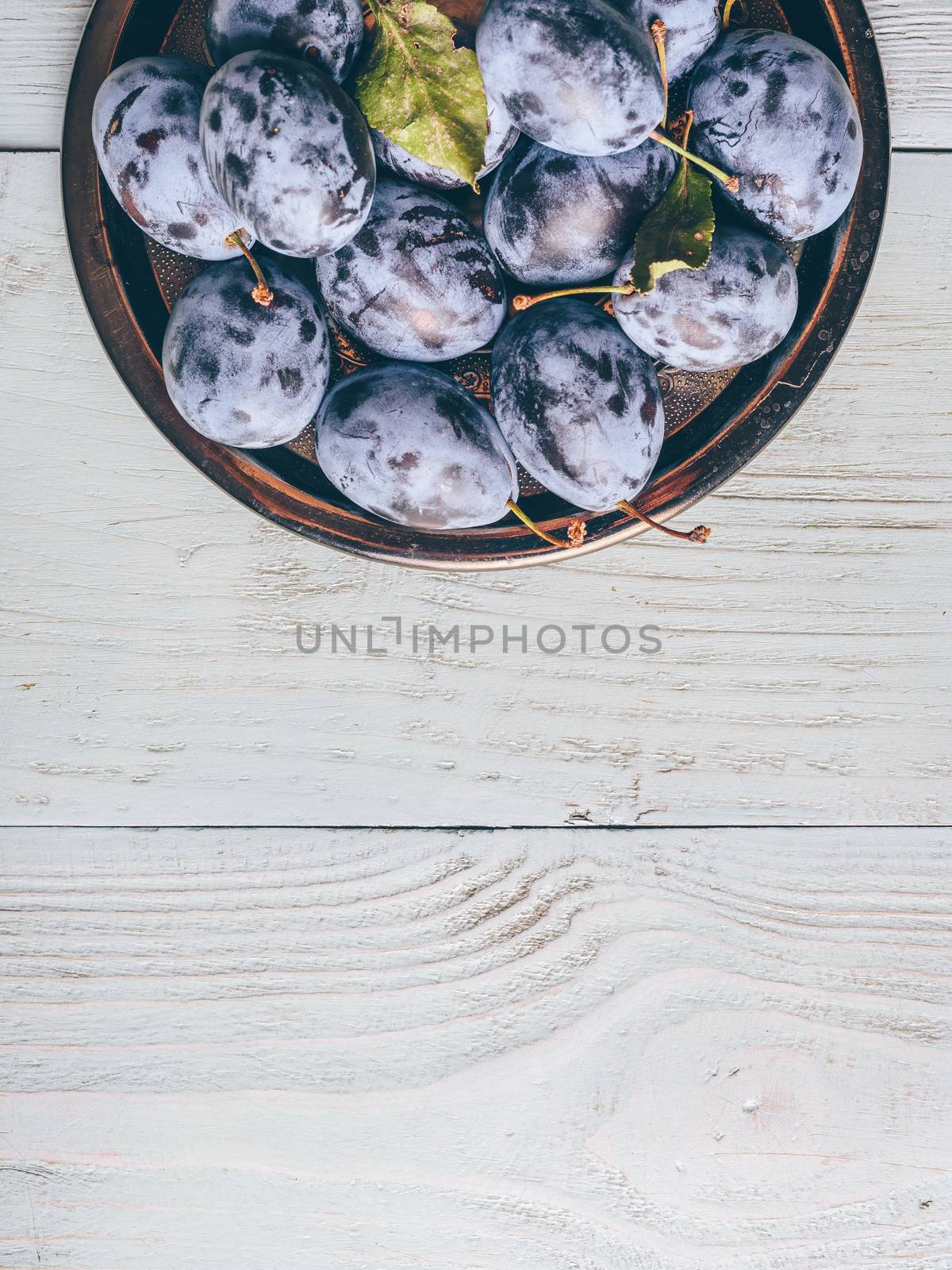 Ripe plums on metal plate over light wooden surface. Copy space