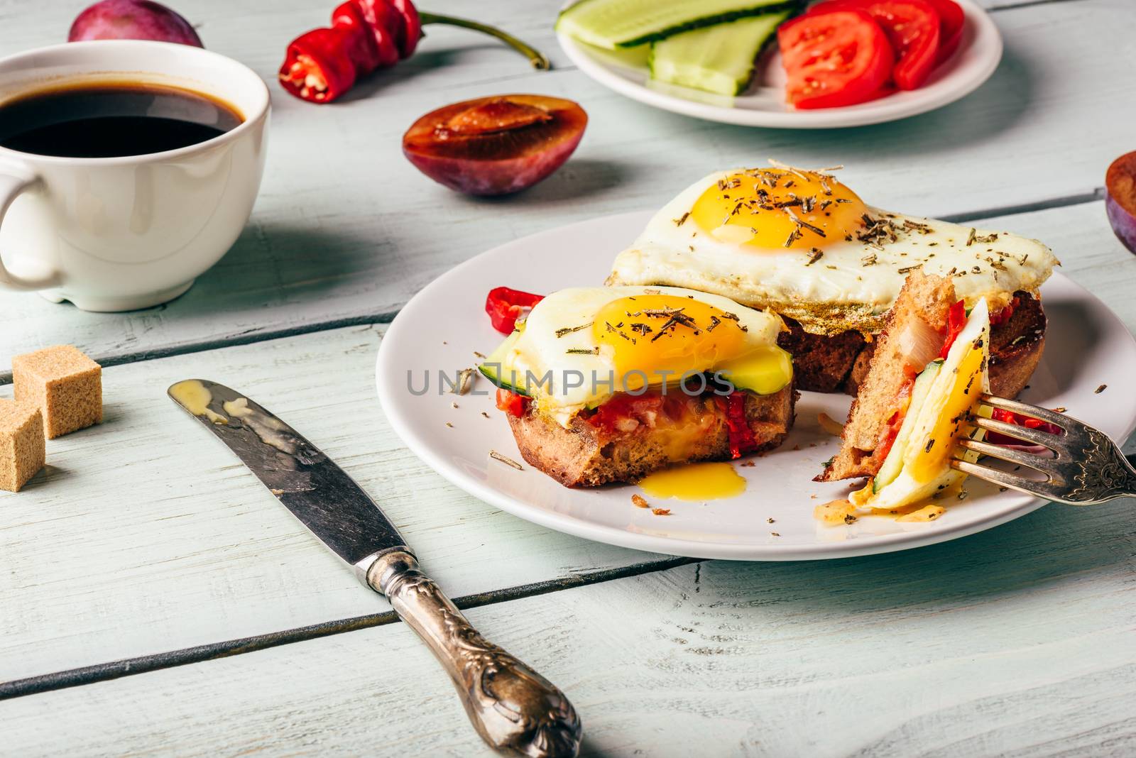 Sandwiches with vegetables and fried egg on white plate, cup of coffee and some fruits over wooden background.