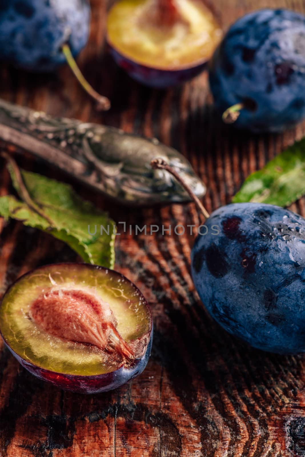 Ripe plums on wooden table with leaves, water drops and vintage knife