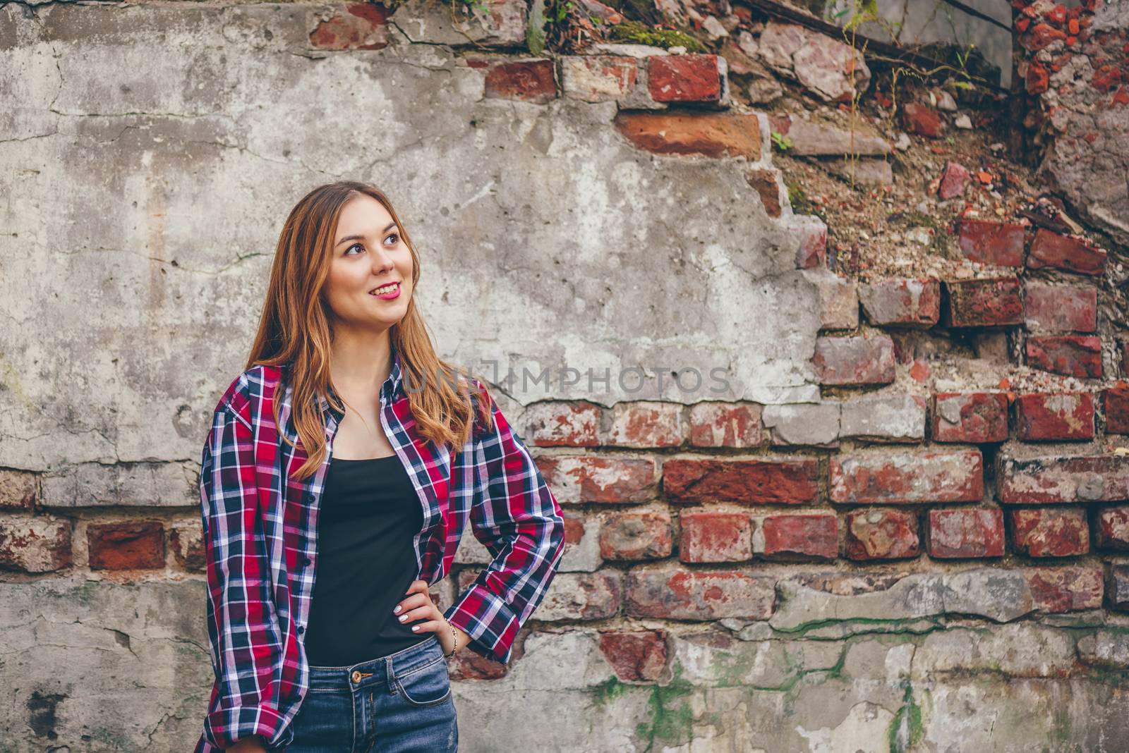 Young beautiful woman is smiling while standing in front of brick wall