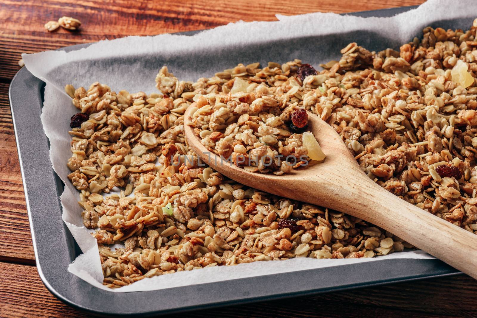 Homemade granola on baking sheet with wooden spoon