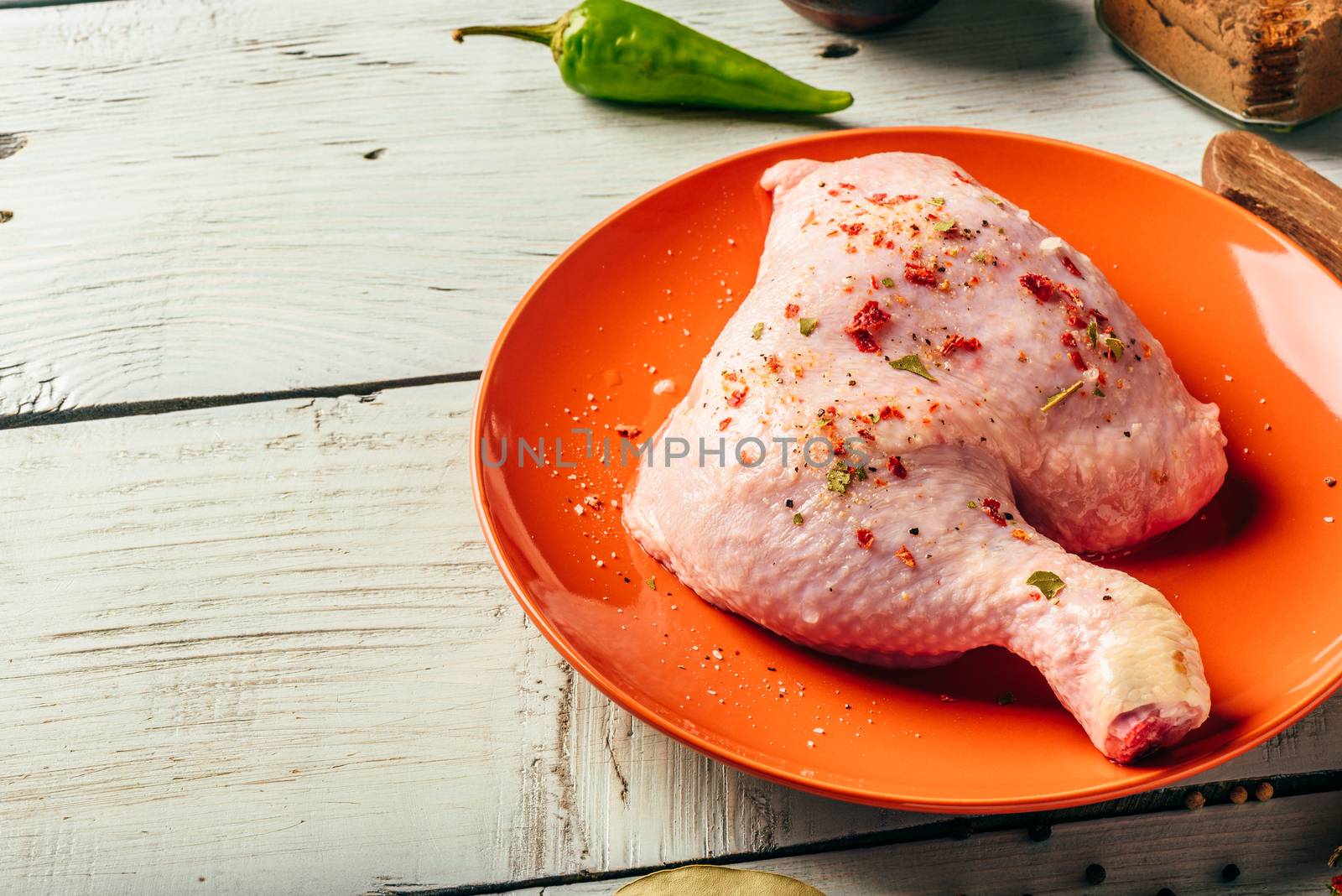 Chicken leg quarter on orange plate over wooden surface with different spices