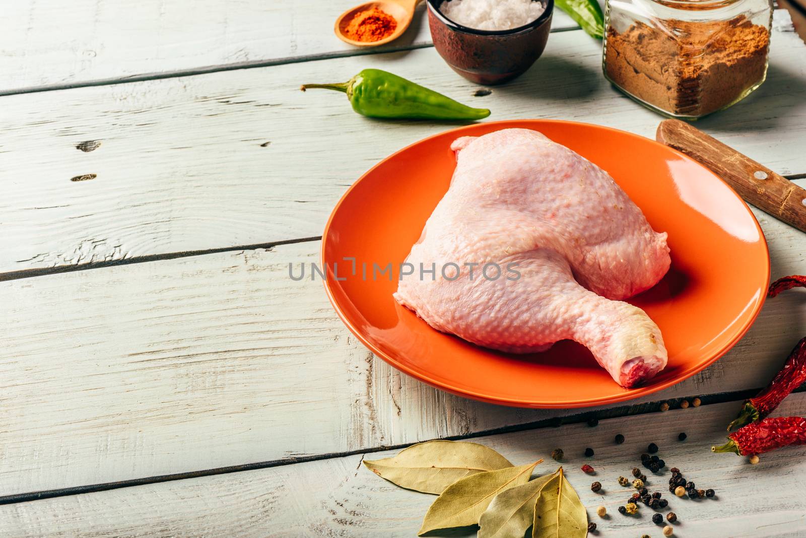 Chicken leg quarter on orange plate over wooden surface with different spices