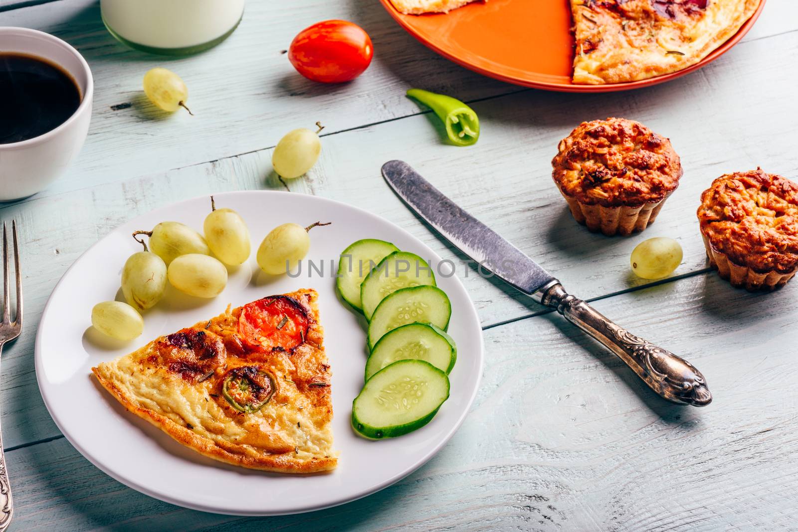 Slice of frittata with cup of coffee, grapes and muffins over light wooden background. Healthy eating concept.