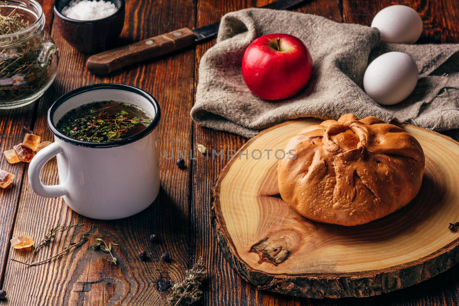 Rustic breakfast with traditional tatar pastry elesh, herbal tea in metal mug, apple and boiled eggs over dark wooden surface