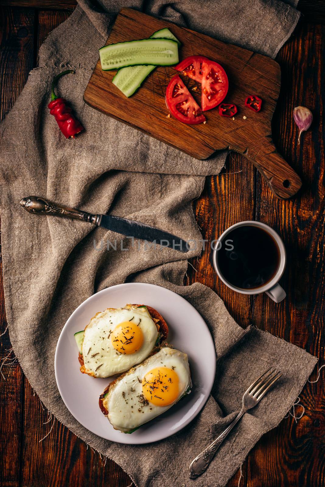 Breakfast toasts with vegetables and fried eggs on white plate and cup of coffee over grey rough cloth. View from above.