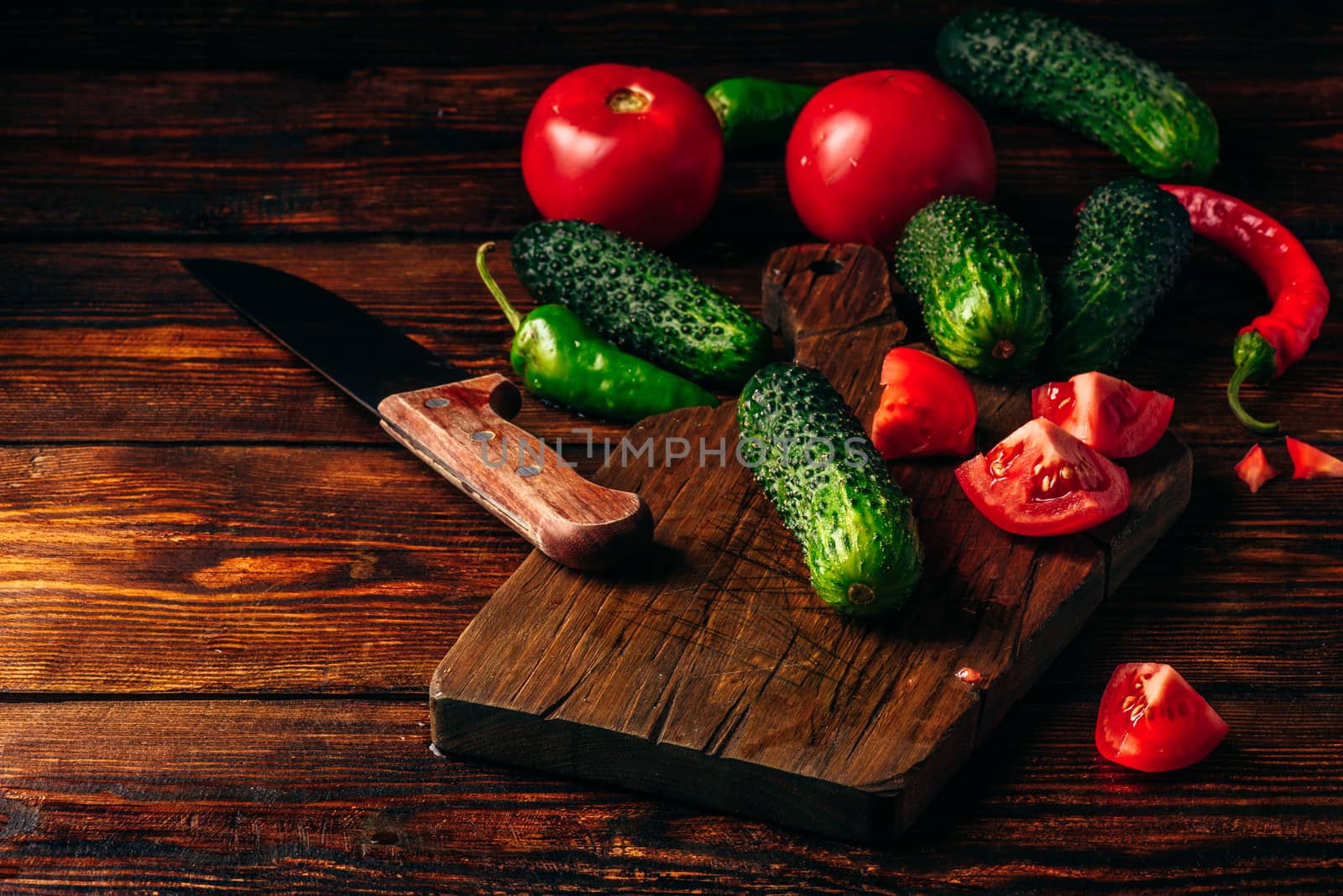 Fresh cucumbers, tomatoes and chili peppers on cutting board for preparing salad.