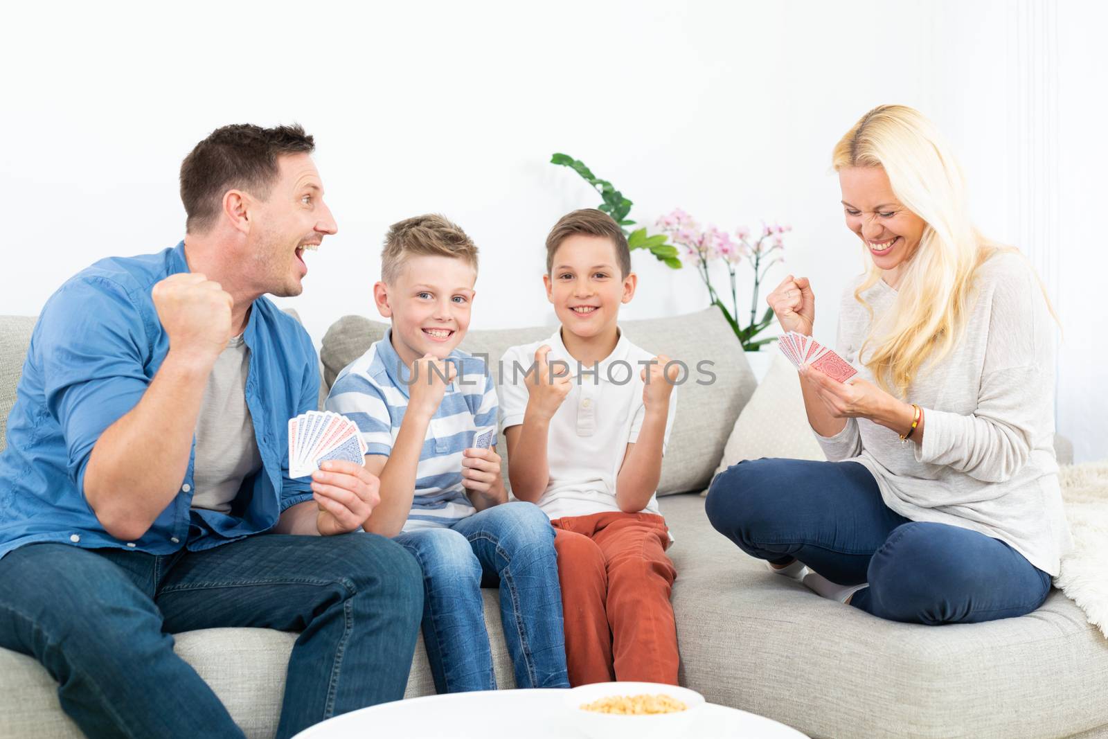 Happy family playing card game on living room sofa at home and having fun together celebrating the game winner.