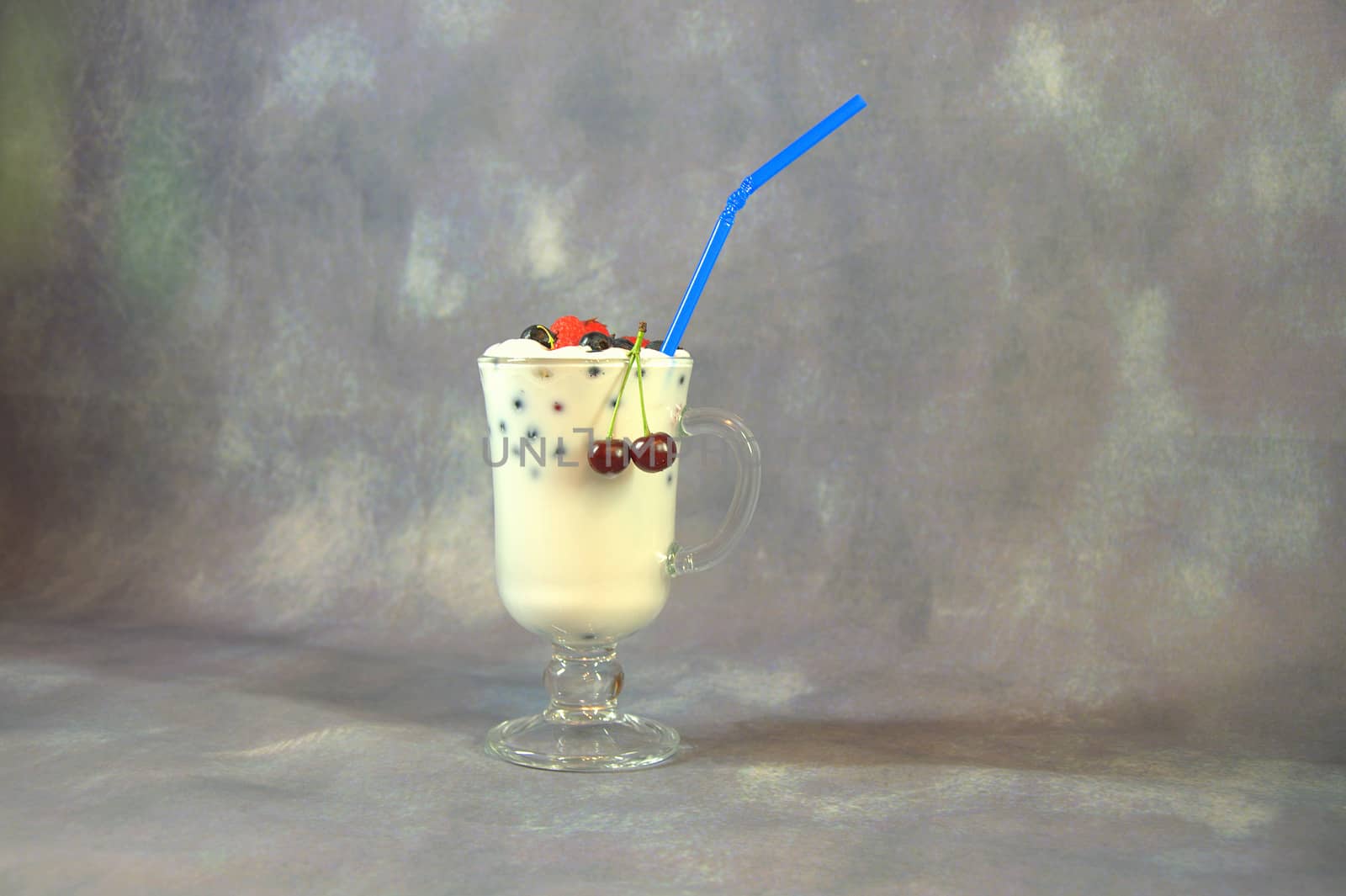 Tall glass cup with milkshakes with a straw and berries.