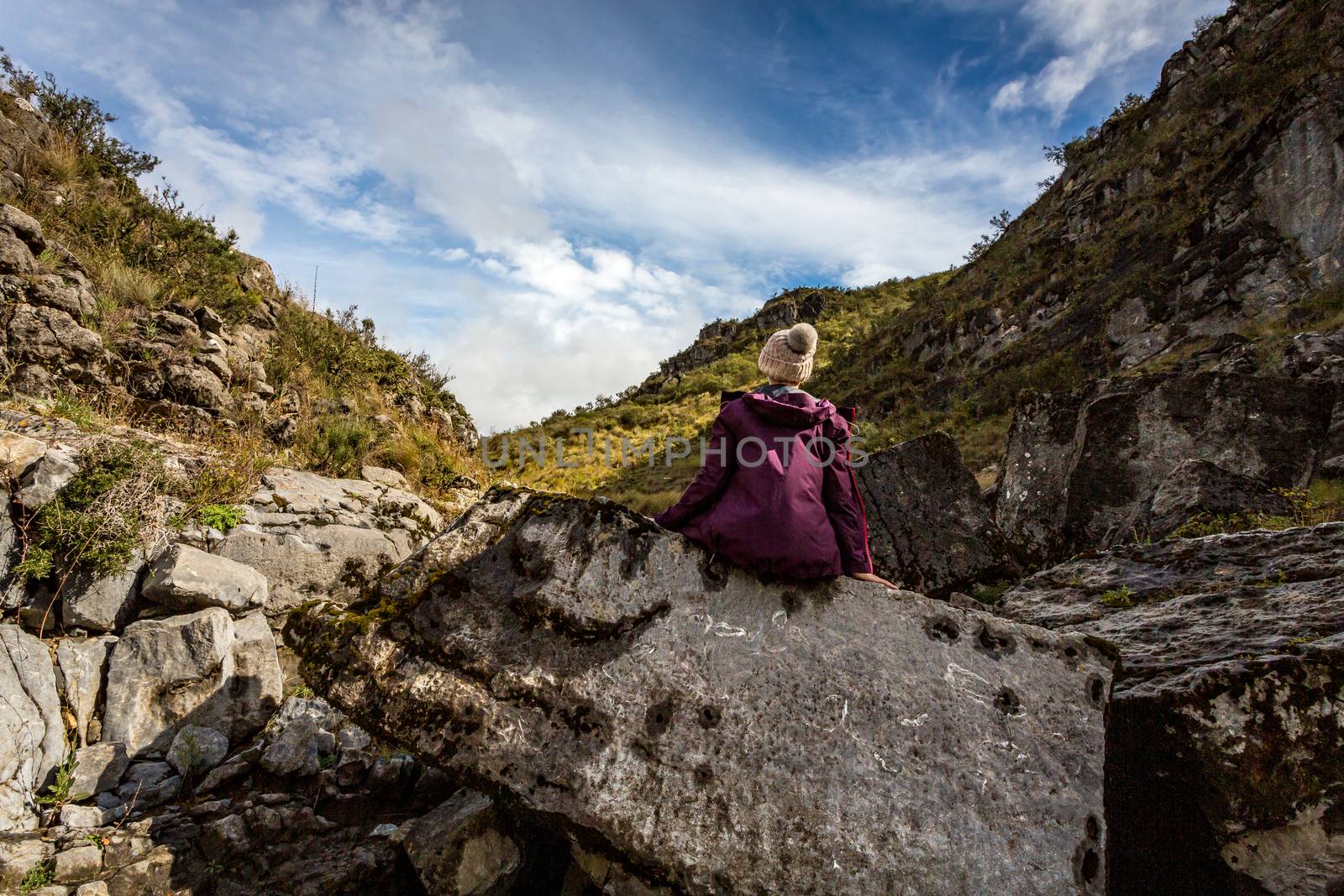 A woman sits on an ancient rock exposed and full of fossils from the sea. The elevation of the land now over 1200 metres above sea level, located in Snowy Mountains Kosciuszko National Park