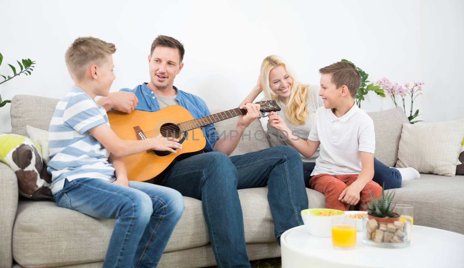 Happy caucasian family smiling while playing guitar and singing songs together at cosy modern home. Spending quality leisure time with children and family concept.